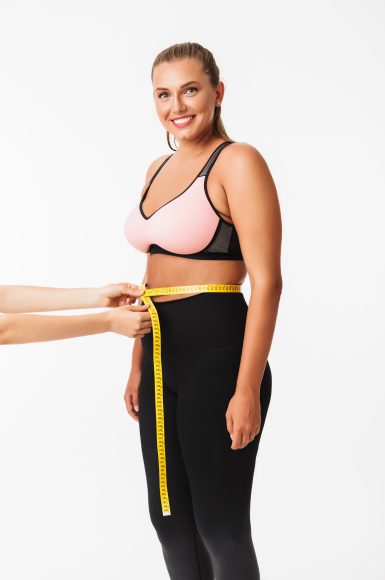 Beautiful smiling girl with excess weight in sporty top measurin