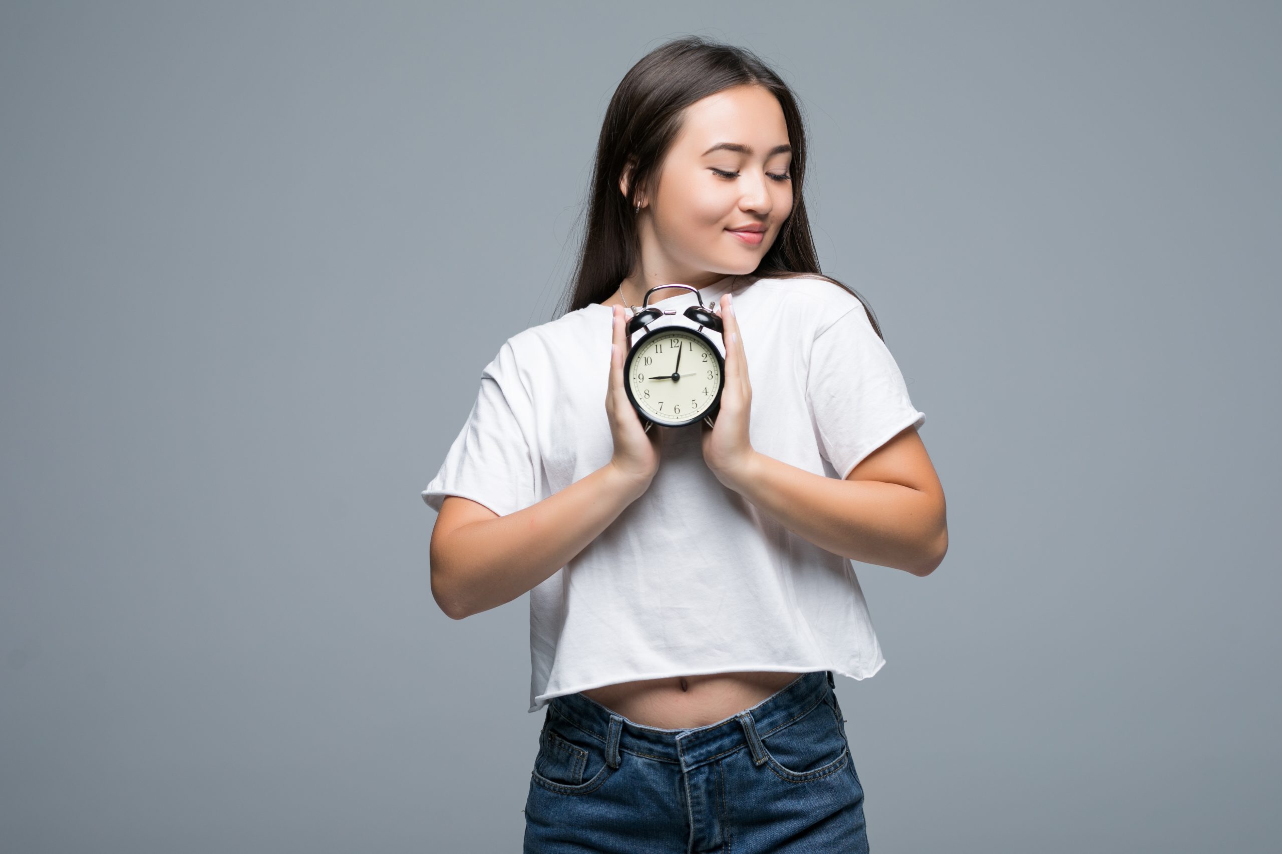 Young Asian woman smile with a clock isolated on gray background