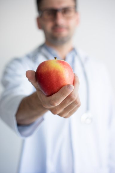 Close-up of doctors hand giving red apple